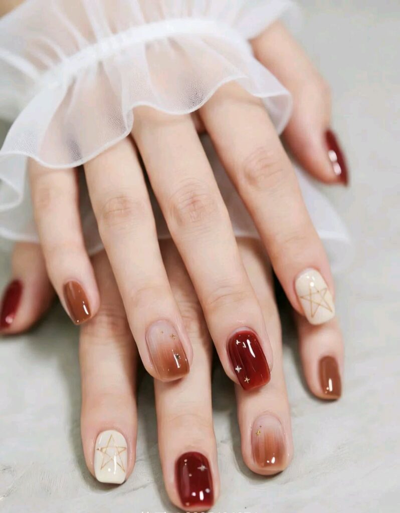 Nail đẹp gam nâu caramel, đỏ mận và kem ombre, điểm xuyết họa tiết ngôi sao kim tuyến, mang phong cách ấm áp nữ tính.