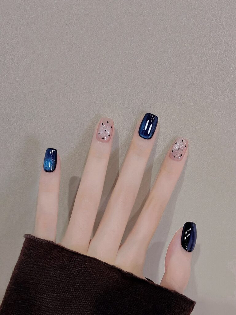 Nail tay đẹp đơn giản với hiệu ứng ánh nhũ cat-eye xanh navy huyền bí, phối nền nude chấm bi trắng đen, phong cách bầu trời đêm.