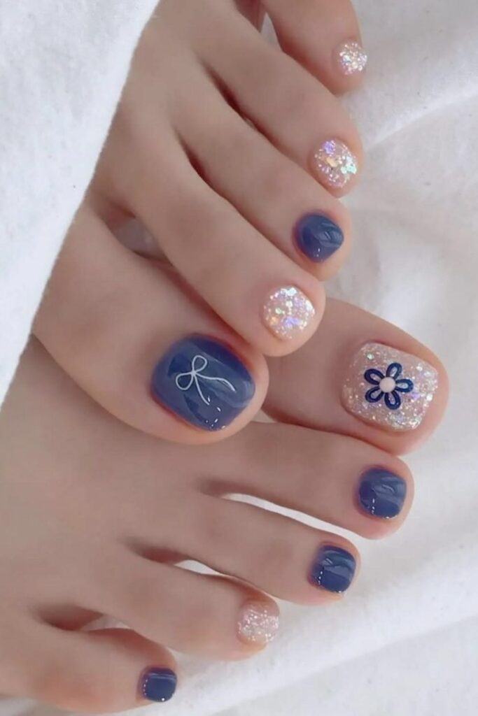 Mẫu nail chân đẹp đơn giản với sắc xanh navy sang phối kim tuyến và họa tiết vẽ nơ, hoa xinh xắn, tinh tế.