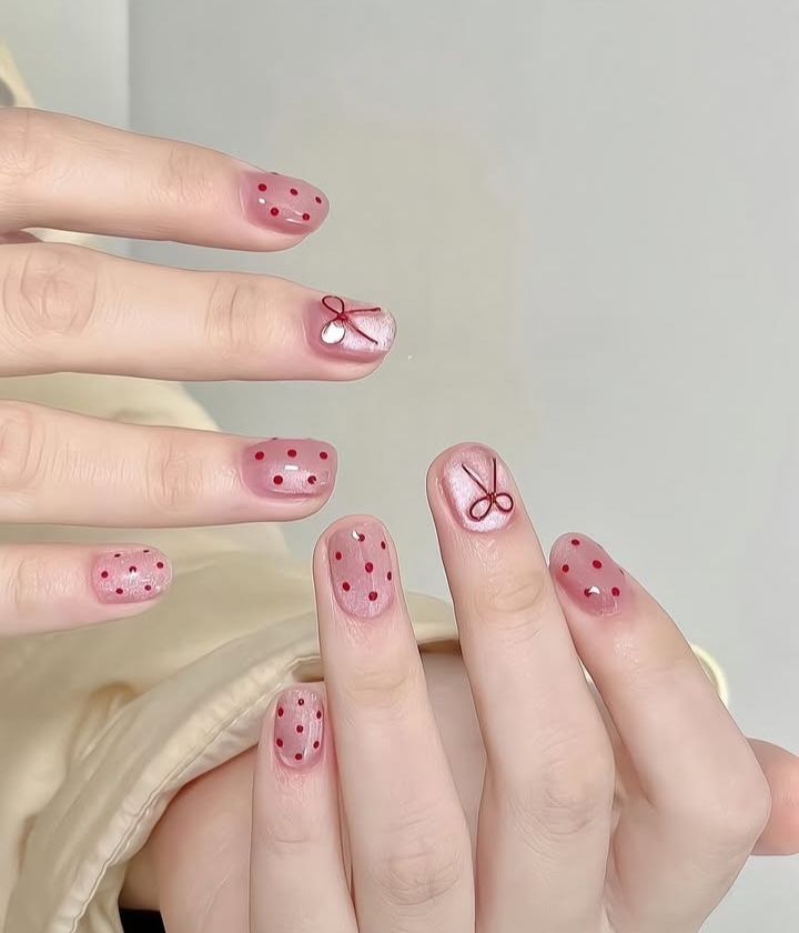Mẫu nail cho móng ngắn nền hồng trong, chấm bi đỏ polka dot và nơ vẽ tay dễ thương, phong cách vintage.