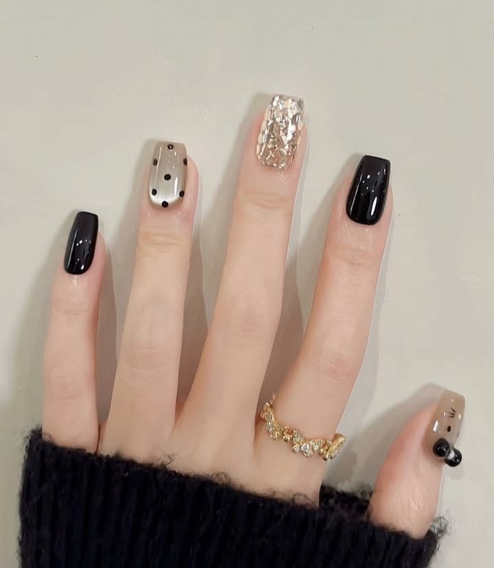 Các mẫu nail đẹp cá tính kết hợp gam đen bóng gương, nhũ vàng foil ánh kim và họa tiết chấm bi trắng đen phá cách, nổi bật.