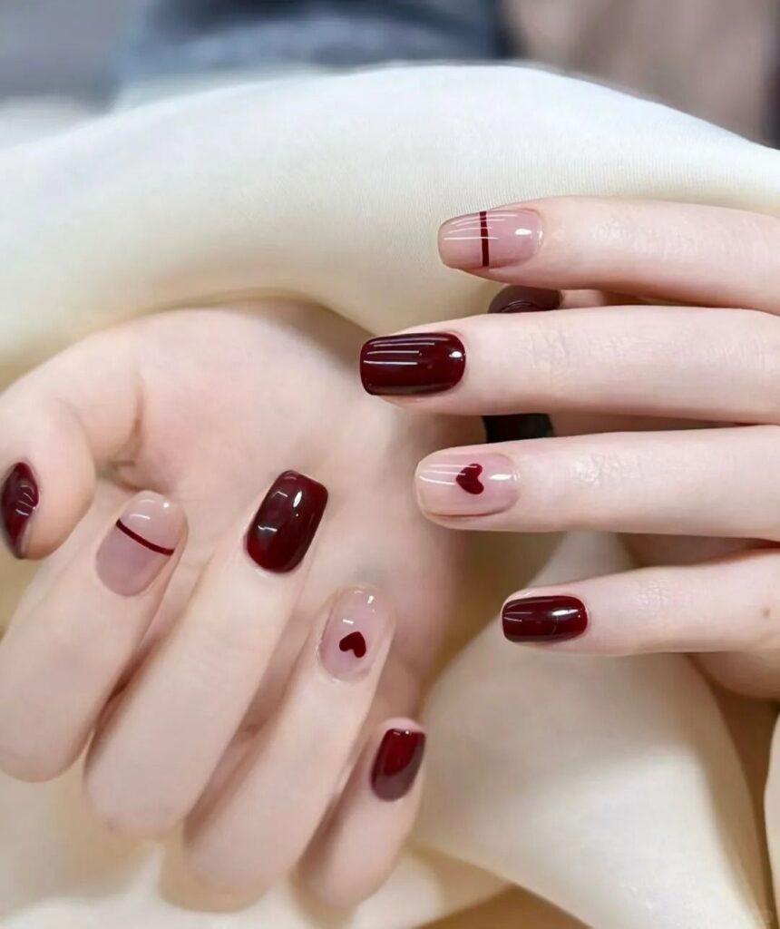 Nail đẹp nhẹ nhàng gam đỏ đô bóng gương phối nền nude, điểm xuyết họa tiết trái tim nhỏ và đường line kẻ mảnh, tinh tế, thanh lịch.
