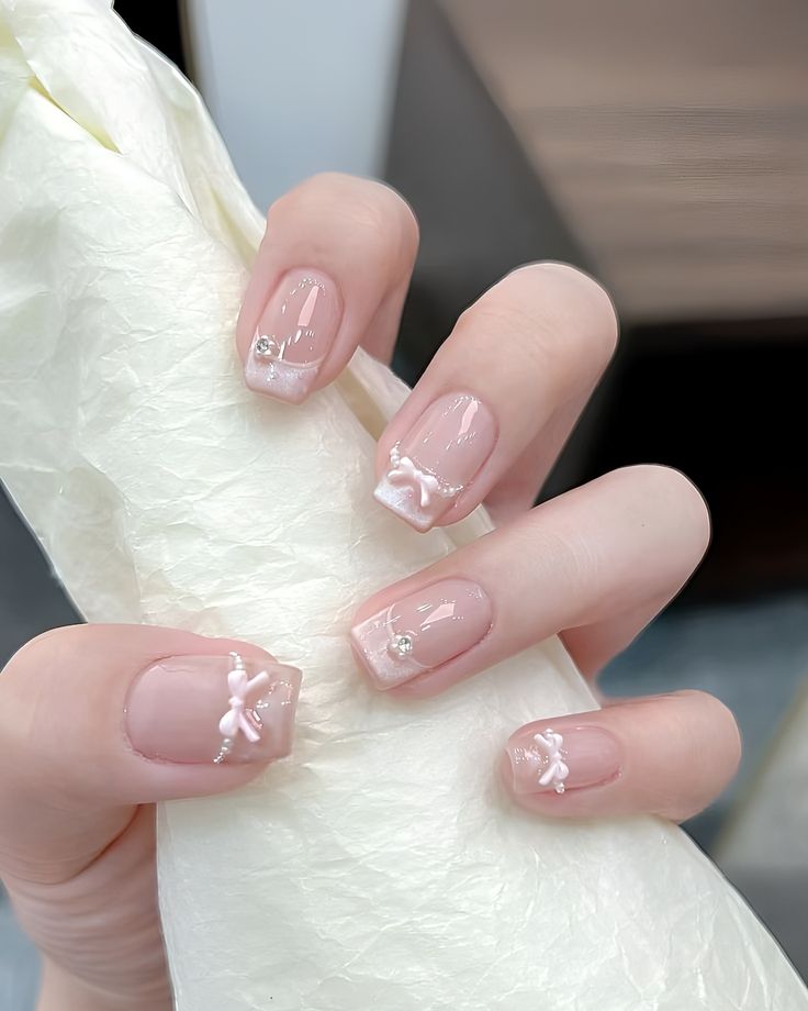Mẫu nail đơn giản cho móng ngắn nền trắng sữa loang, đính nơ nổi 3D và đá li ti, nhẹ nhàng thanh tao.