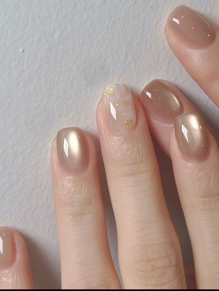 Mẫu nail mắt mèo đẹp phối tông be vàng ánh kim lấp lánh, một móng nền trắng sữa điểm nhũ vàng nhỏ tinh tế, hoàn thiện bóng gương sang trọng.