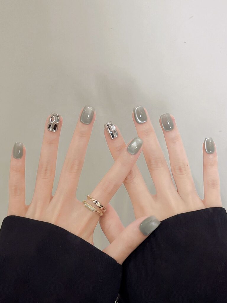 Mẫu nail mắt mèo đính đá tông xám khói dịu mắt, hai móng điểm đá pha lê 3D lớn lấp lánh, tạo hiệu ứng sang trọng và nổi bật.