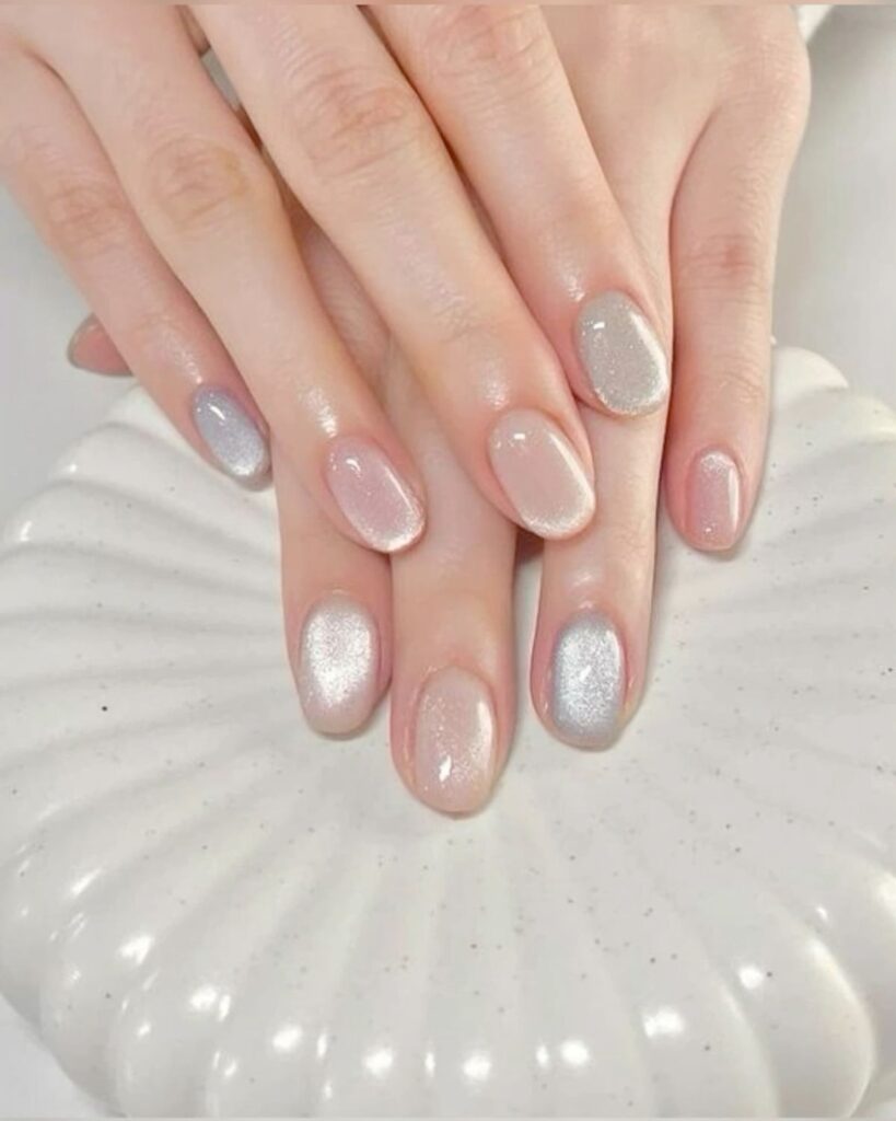 Mẫu nail mắt mèo nhũ bạc lấp lánh phối cùng các móng nude hồng nhẹ nhàng, đặt trên nền đĩa hình vỏ sò trắng, tạo cảm giác tinh khôi.