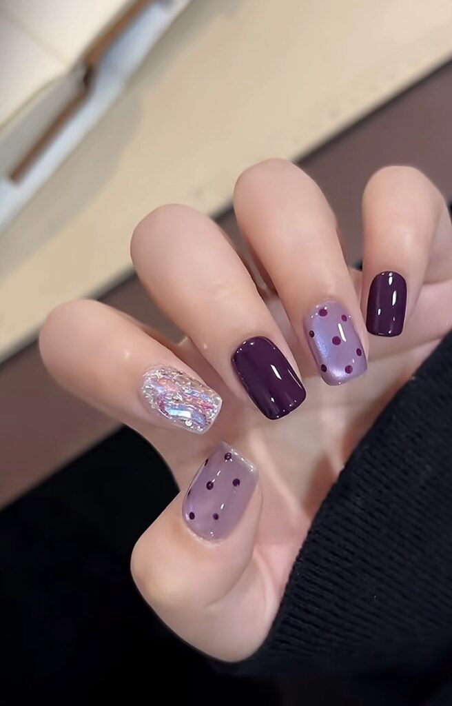 Mẫu nail mắt mèo sang trọng tông tím than đậm bóng gương, phối cùng móng nhũ vỡ (foil) ánh kim lấp lánh và họa tiết chấm bi tím, quý phái.