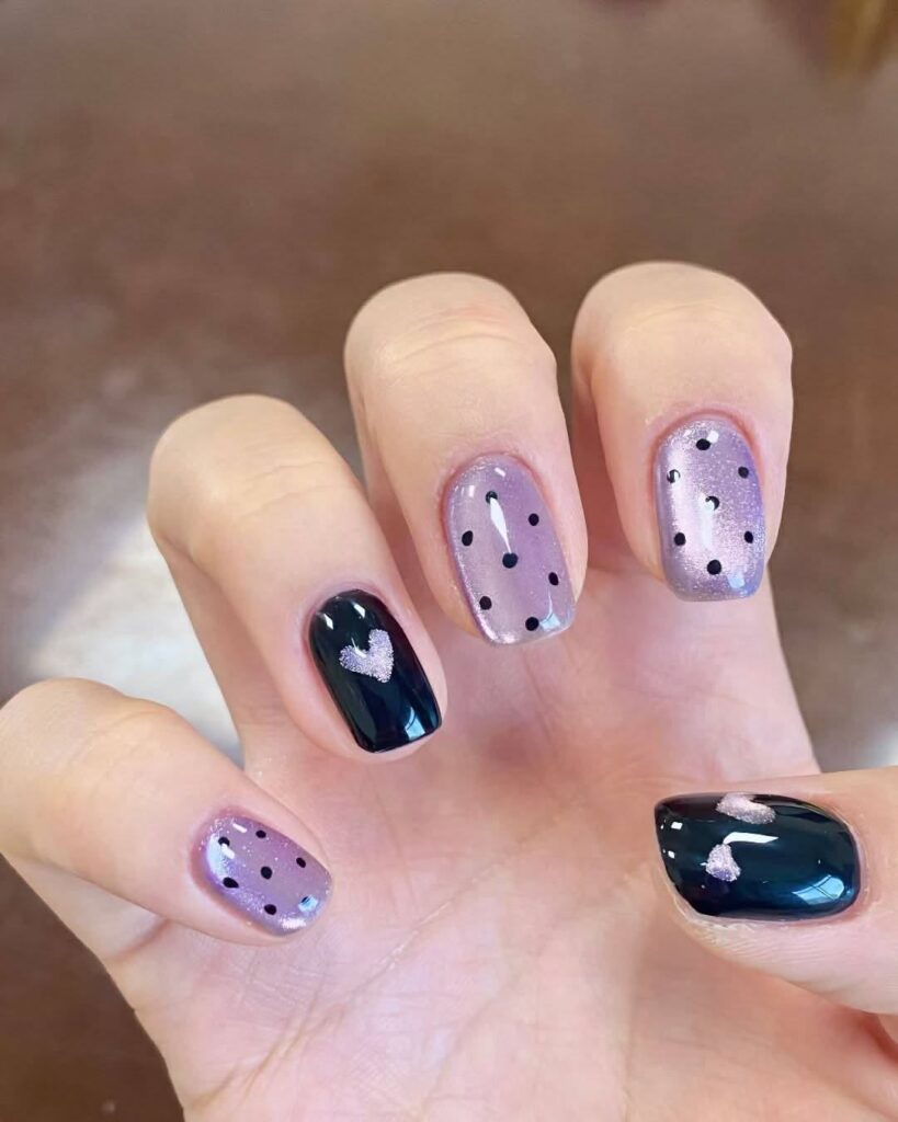 Mẫu nail mắt mèo tím lavender nhẹ nhàng, phối họa tiết chấm bi đen và một móng đen tuyền đính trái tim ánh nhũ, cá tính nổi bật.
