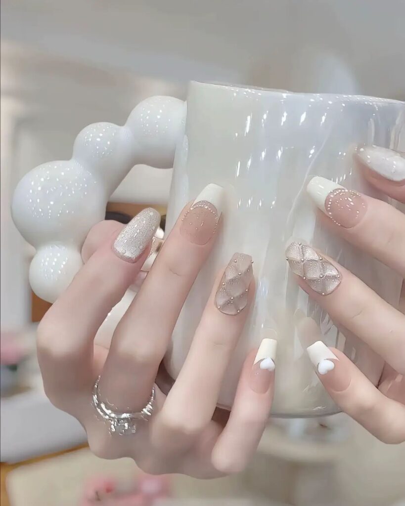 Mẫu nail màu trắng đẹp dáng coffin nền nude - be, họa tiết chần bông và ren trắng đính hạt ngọc li ti, điểm French tim trắng tinh tế.