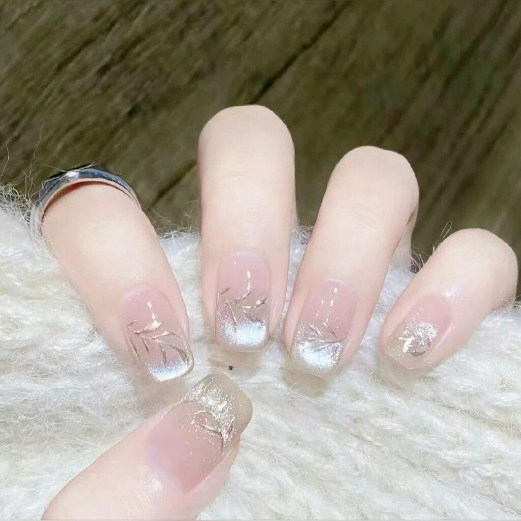 Mẫu nail màu trắng đẹp nền nude hồng, hiệu ứng mắt mèo ánh bạc kết hợp họa tiết lá, cành nhũ vàng ánh kim sang chảnh.