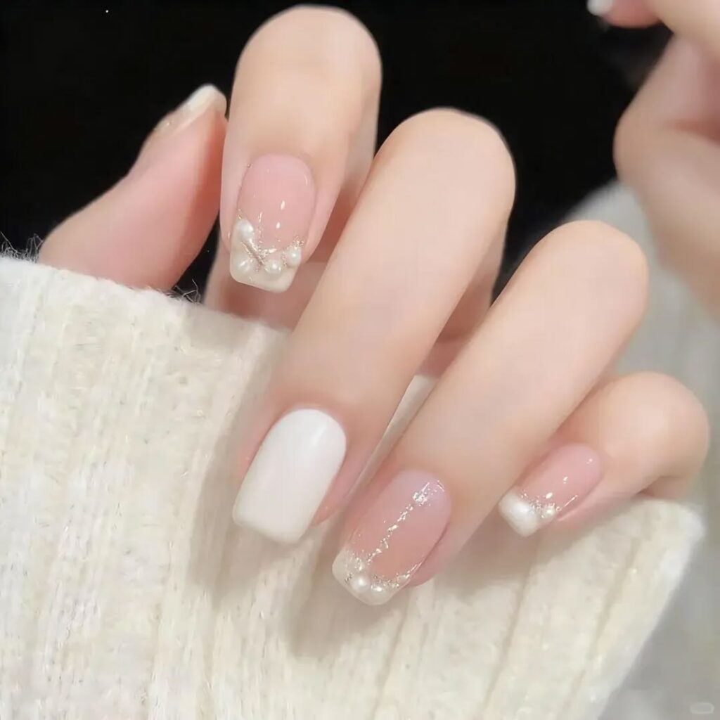 Mẫu nail màu trắng nền nude hồng và trắng sữa, đính ngọc trai cùng nhũ vàng ánh kim ở chân móng, sang trọng và quý phái.