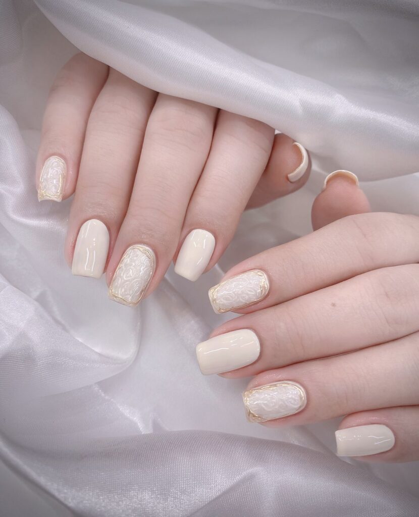 Mẫu nail màu trắng tông trắng ngà - kem bóng, điểm móng đắp họa tiết chạm nổi viền nhũ vàng, cổ điển và sang trọng.