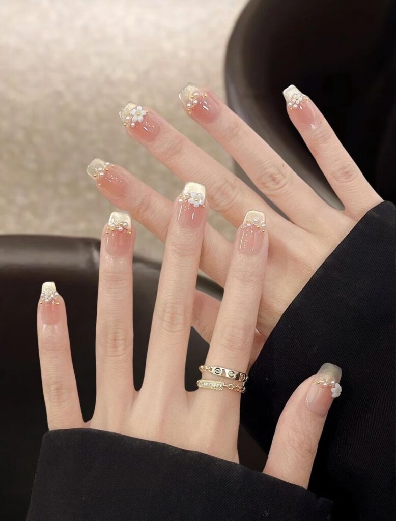 Những mẫu nail đẹp cho móng dài sang chảnh, hot nhất 2026 3 Mẫu nail móng vuông dài nền nude, đầu phủ nhũ vàng, đính hoa trắng 3D, ngọc trai và hạt vàng, sang trọng cho nail cô dâu.
