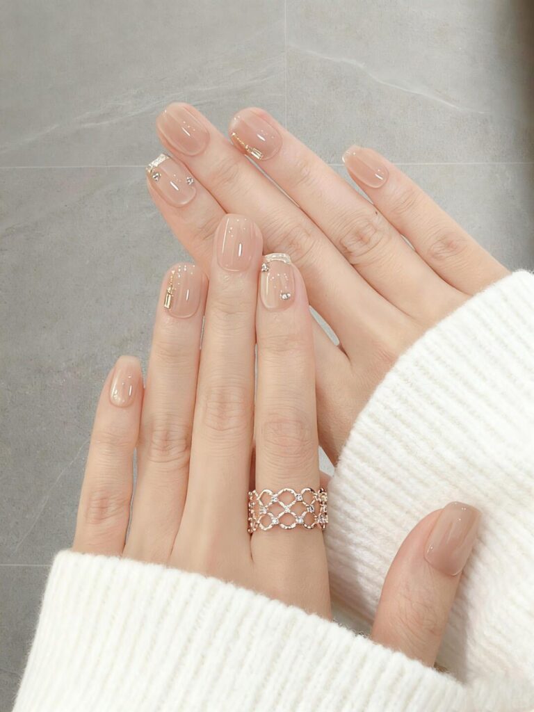 Mẫu nail sơn thạch đính đá nền nude sữa trong veo, điểm nhũ vàng và hạt đá li ti, tối giản sang trọng.