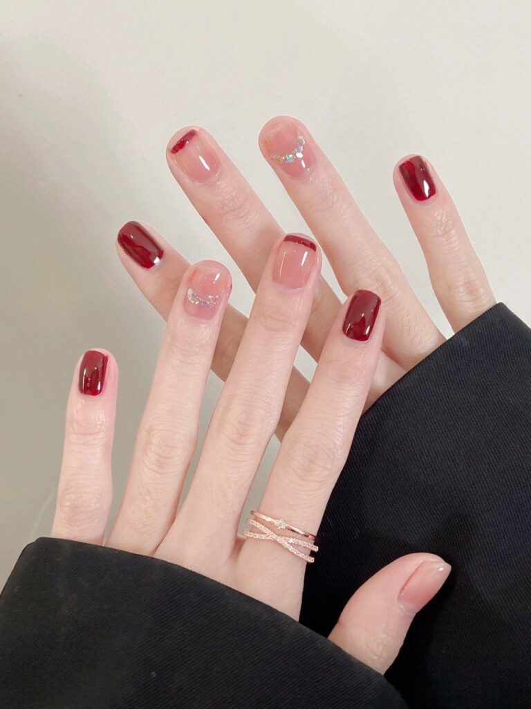 Nail tay đơn giản đẹp kiểu French tip đỏ đô nửa đầu móng trên nền nude trong suốt, điểm đá nhỏ tinh xảo, thanh lịch và cuốn hút.