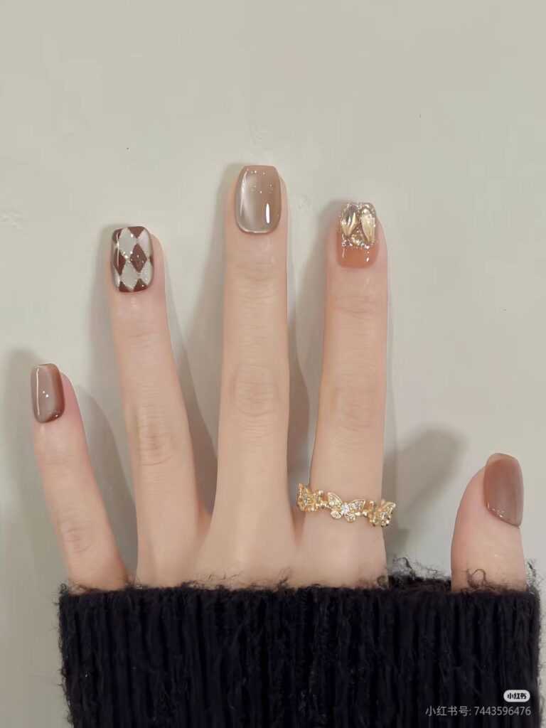 Mẫu nail tay đẹp gam nâu socola trầm ấm, phối họa tiết caro (argyle) trắng nâu và đính đá 3D ánh vàng nổi bật, sang trọng.