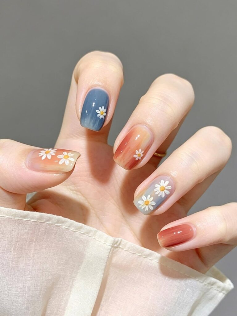 Móng nail đẹp phối ombre nhiều tông xanh, cam, đỏ đất mềm mại, điểm xuyết họa tiết hoa cúc trắng vẽ tay theo phong cách bohemian.