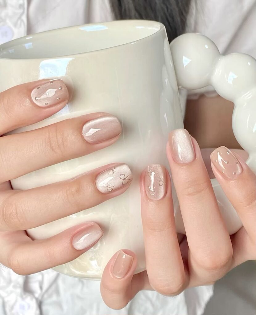Nail màu trắng đẹp dáng ngắn nền trắng sữa mắt mèo, điểm họa tiết nơ nhỏ cùng tông và vài hạt đá li ti, nhẹ nhàng nữ tính.
