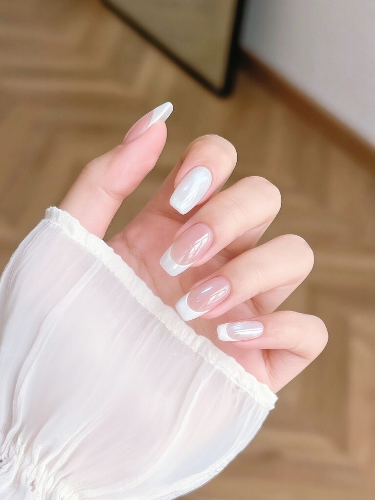 Nail màu trắng dáng coffin nền trong, đầu móng French trắng phủ hiệu ứng bóng óng ánh, sang và hiện đại.