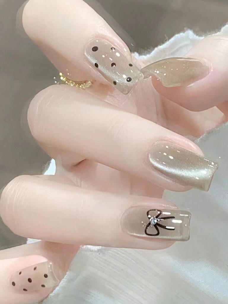 Mẫu nail màu trắng đẹp dáng coffin nền trong ánh nhũ mắt mèo, điểm họa tiết nơ đen và chấm bi đen sang chảnh, cá tính.