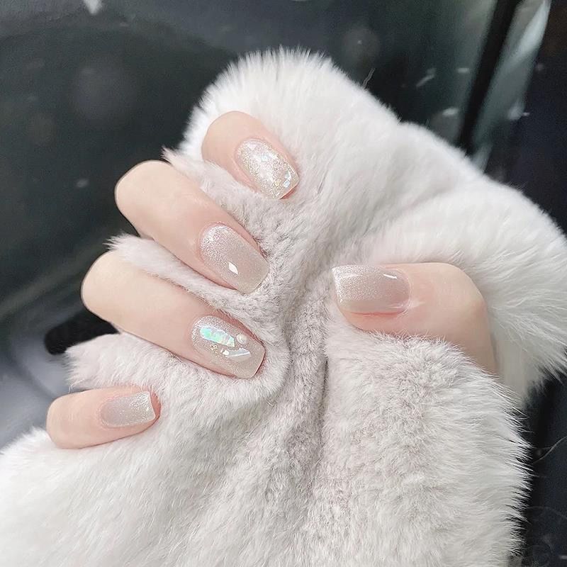Nail màu trắng dáng vuông nền trắng sữa phủ hiệu ứng tráng gương ánh xà cừ, điểm mảnh vỏ ốc ánh bảy màu lấp lánh nổi bật.