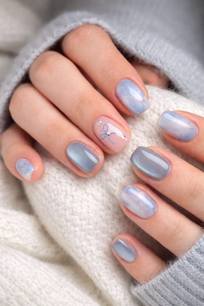 Mẫu nail màu xanh dương đẹp phủ ánh ngọc trai loang marble, điểm nail nude vẽ nơ xanh và đá nhỏ xinh xắn, nữ tính.