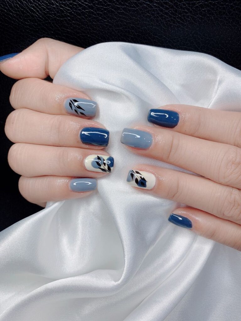 Mẫu nail màu xanh dương phối nhiều sắc xanh cùng nail kem vẽ nhành lá đen, tạo nét nghệ thuật nhẹ nhàng, thanh lịch.