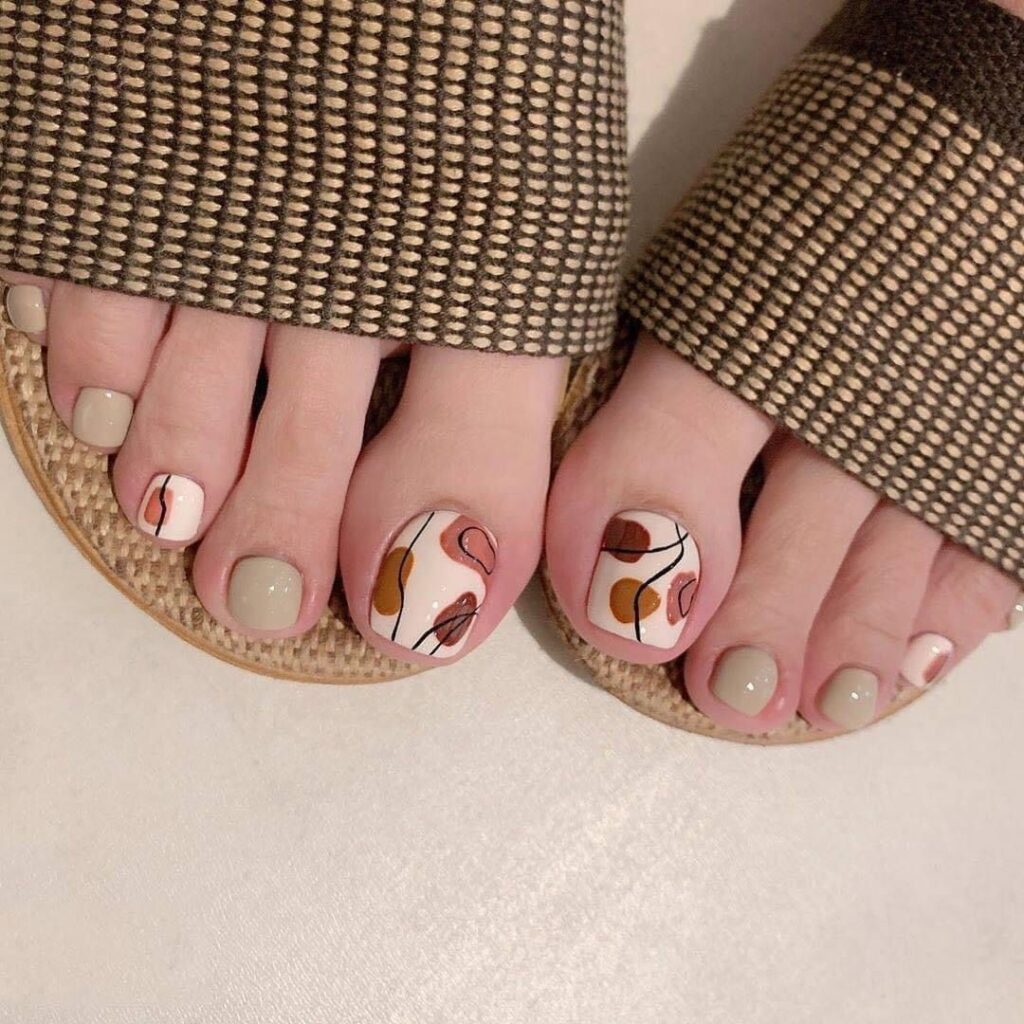 Những mẫu nail chân đẹp đơn giản với nền trắng phối họa tiết trừu tượng tông nâu cam nghệ thuật, trẻ trung.