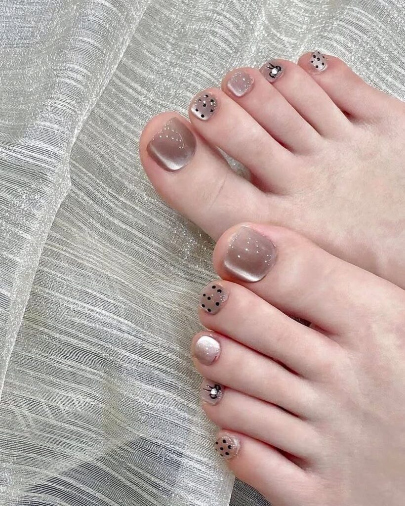 Những mẫu nail chân đơn giản mà đẹp với nền nude trong điểm chấm bi đen và đá nhỏ tinh tế, nhẹ nhàng.